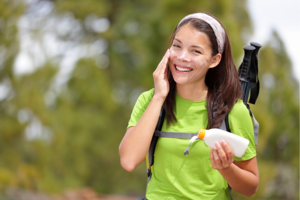 Una mujer joven aplica bloqueador solar en su cara mientras sonríe.