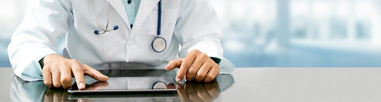 A health care provider sits at a desk and uses a tablet.