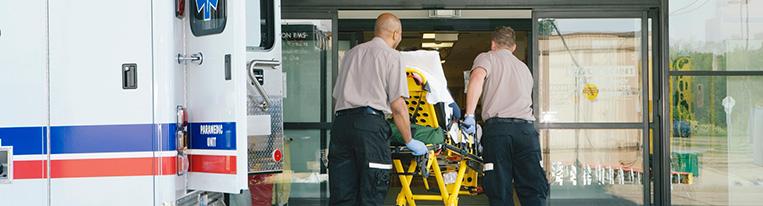 Two paramedics wheel a person on a stretcher into a hospital.