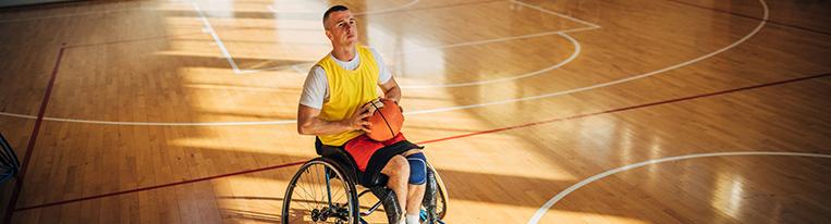 A man in a wheelchair on an indoor basketball court prepares to shoot a basket.