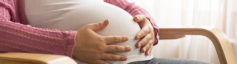 A pregnant woman sitting in a chair touches her belly.