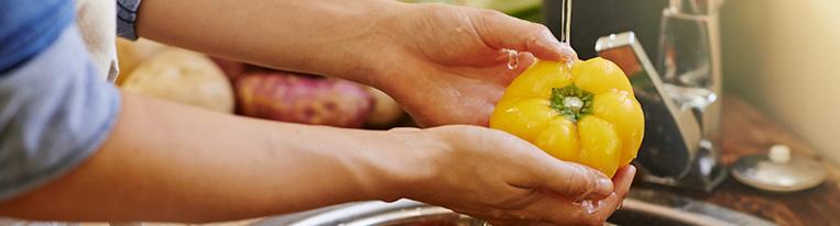 A person washes a yellow bell pepper under a kitchen faucet.