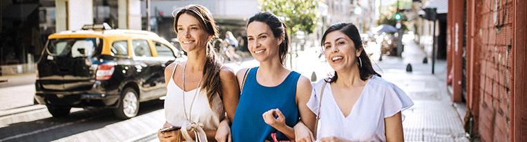 Three women holding shopping bags walk along a city street together.