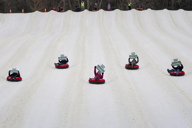 A group of people hold signs while tubing down a snowy hill.