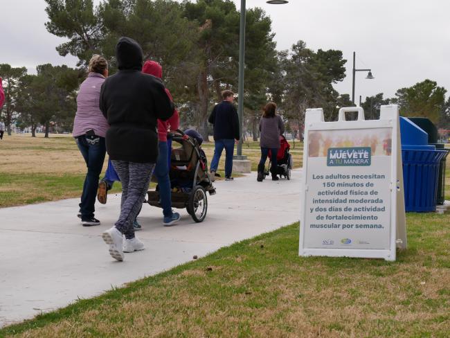 A group of people, one pushing a stroller, pass a sign for a Move Your Way event as they walk in.