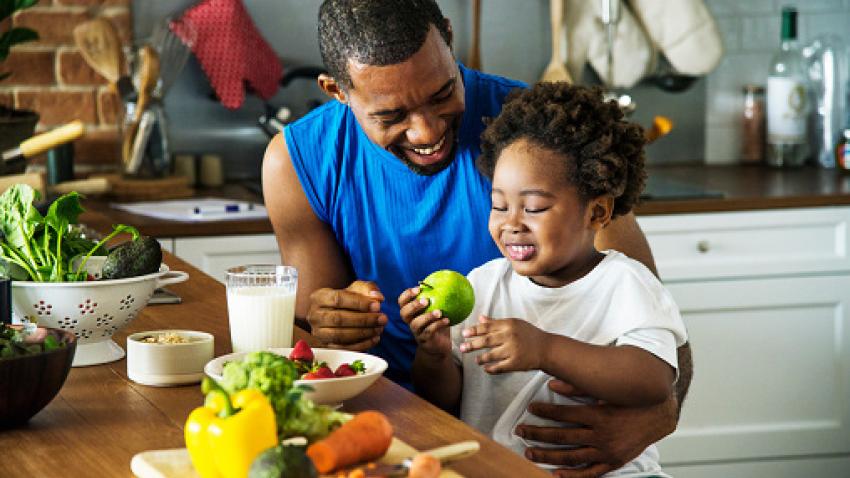 Father and child sitting down with a meal of fresh produce.