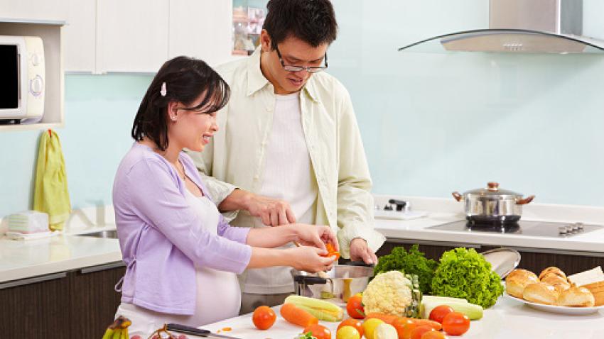 A man and pregnant woman preparing healthy produce for a meal.