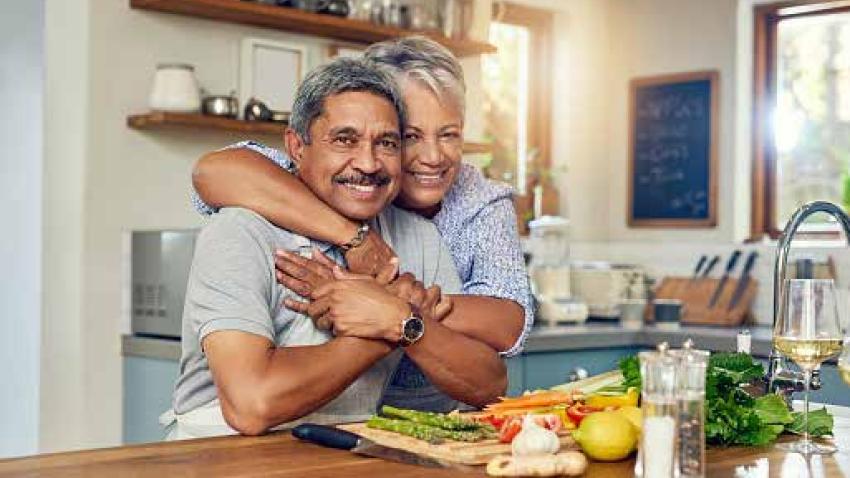 A couple hugs in their kitchen while smiling towards the camera.